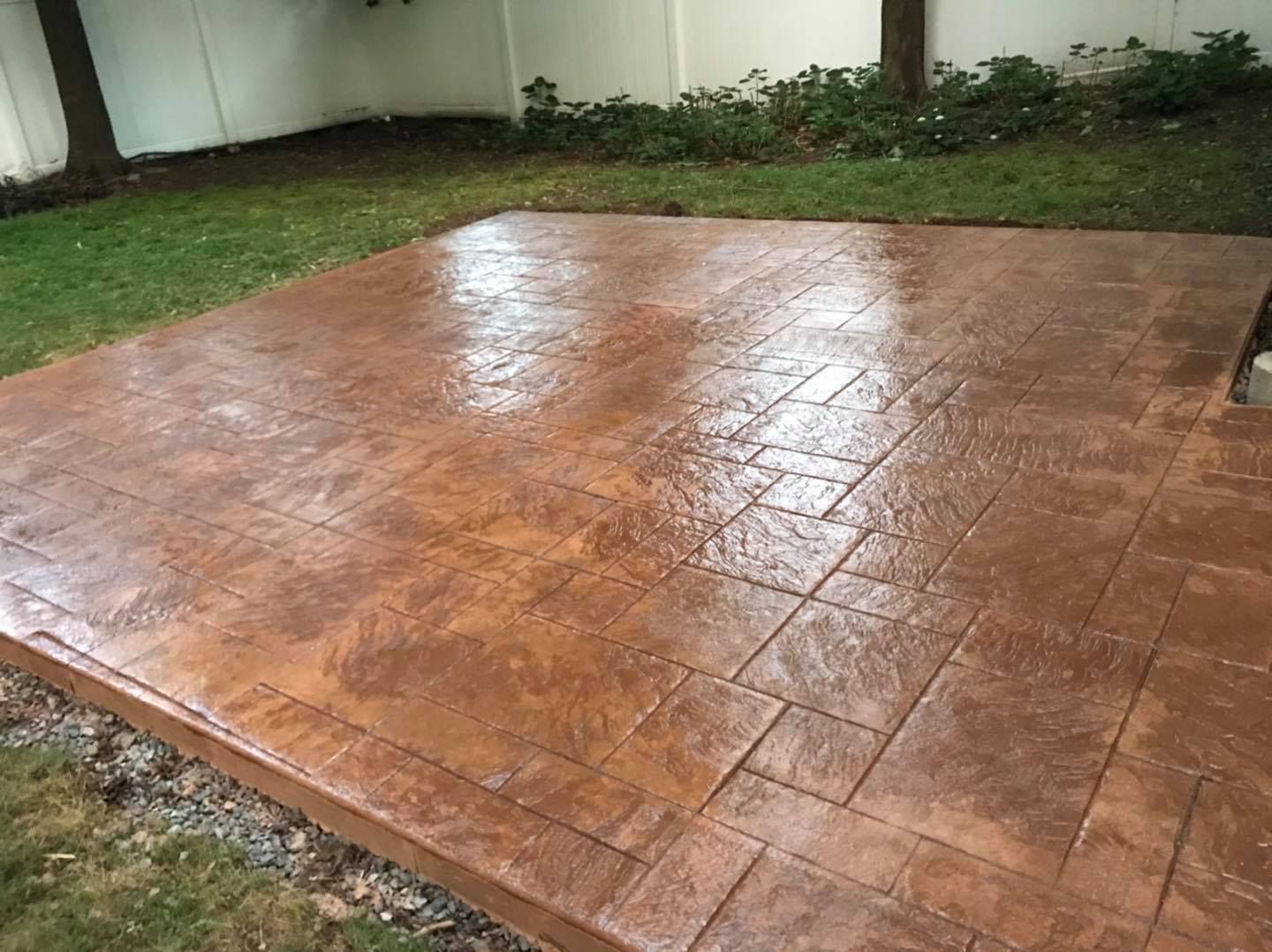 A concrete patio with a brick pattern and a fence in the background.