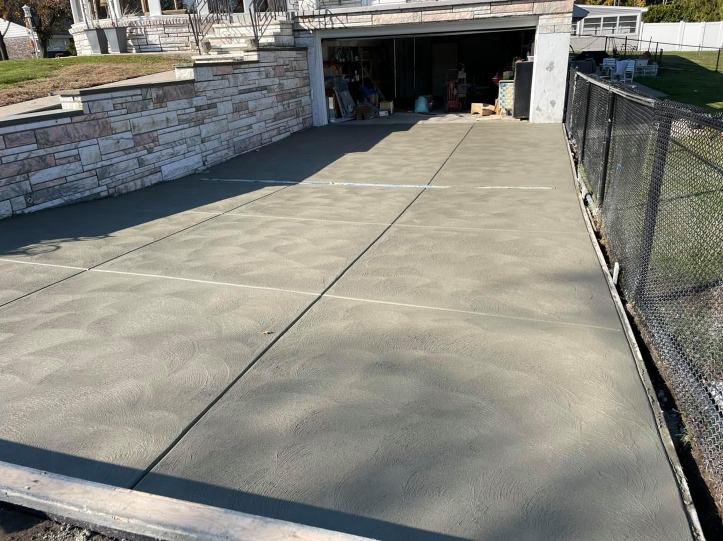 A concrete driveway leading to a garage next to a fence.