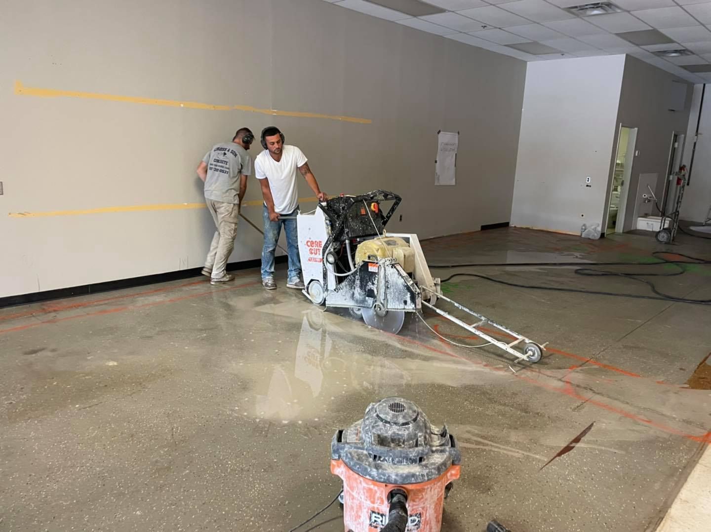 Two men are standing next to a concrete saw in a room.