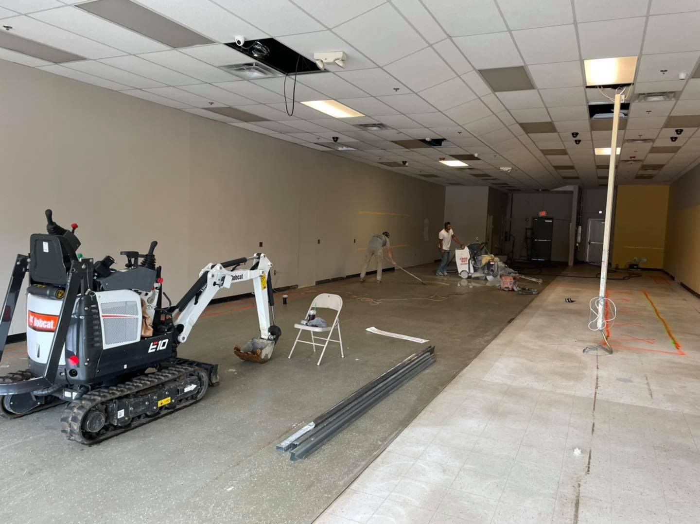A small excavator is sitting in the middle of an empty room.