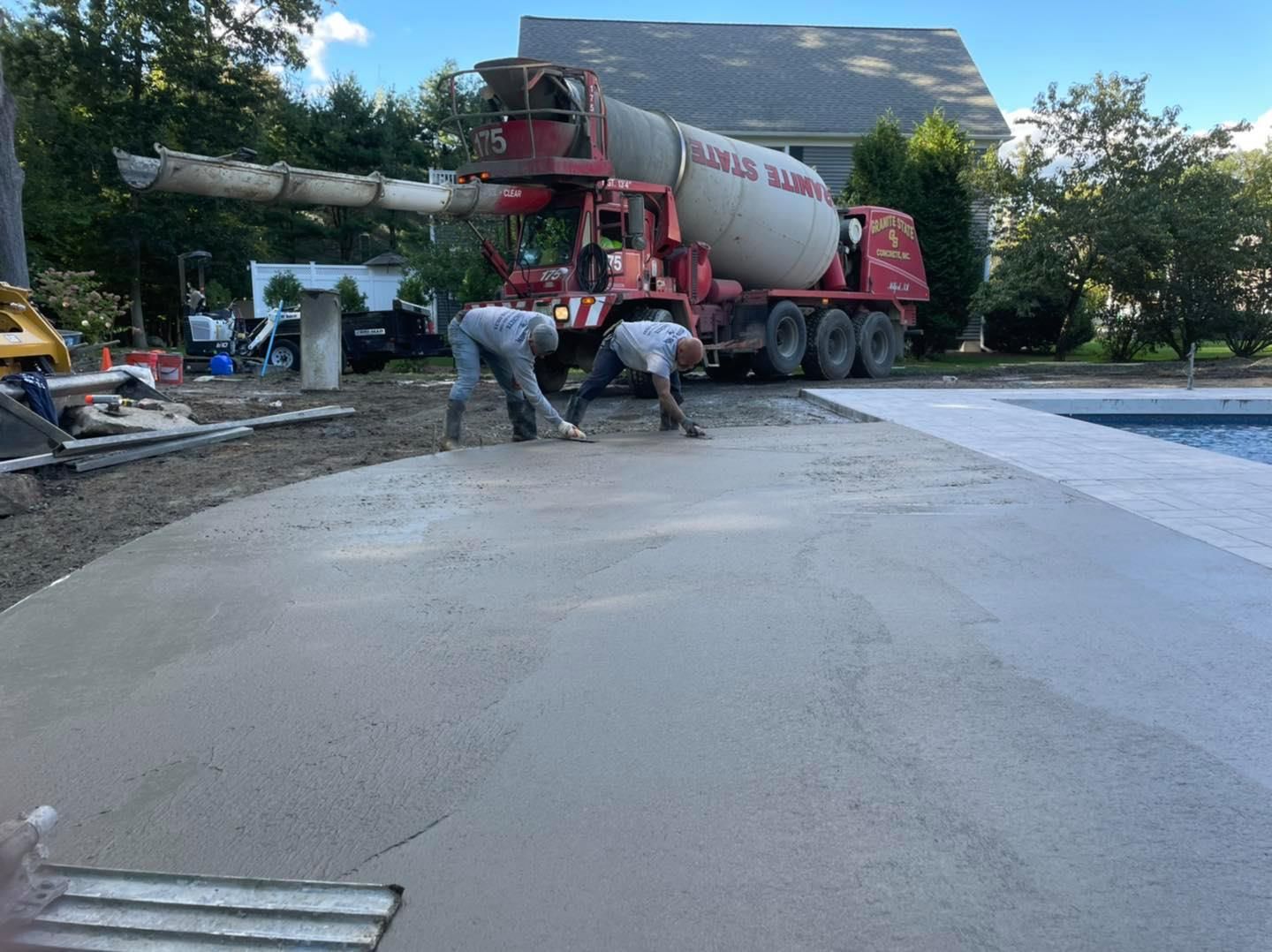 Two men are working on a concrete driveway next to a concrete mixer truck.