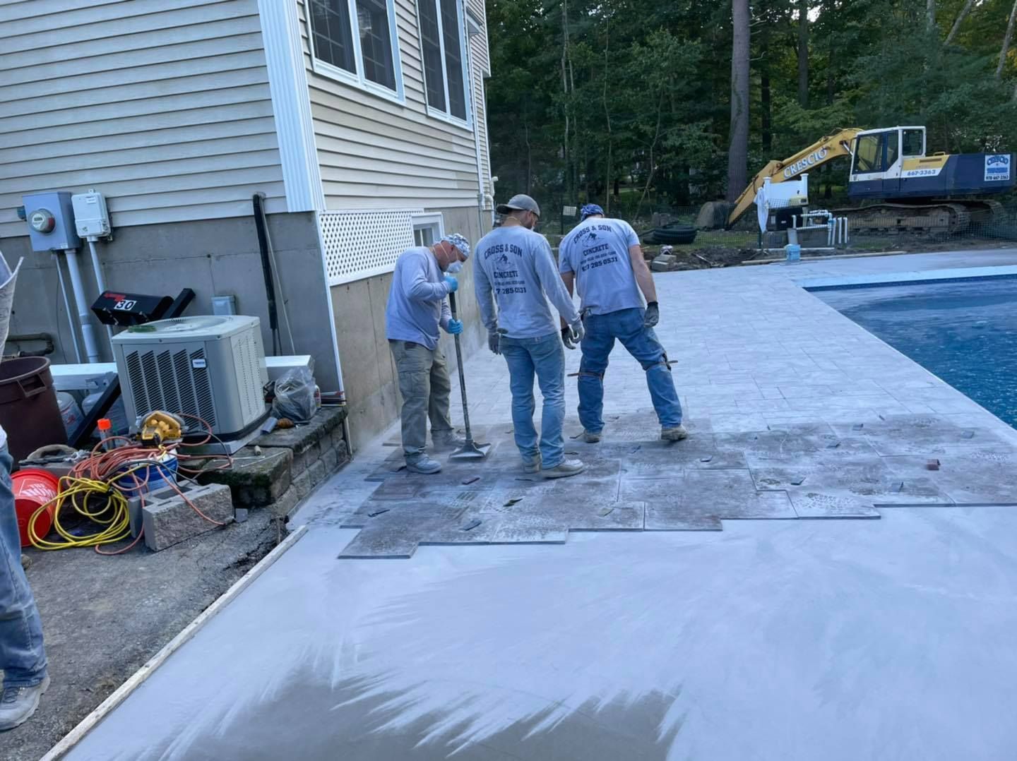Three men are working on a concrete patio next to a pool.