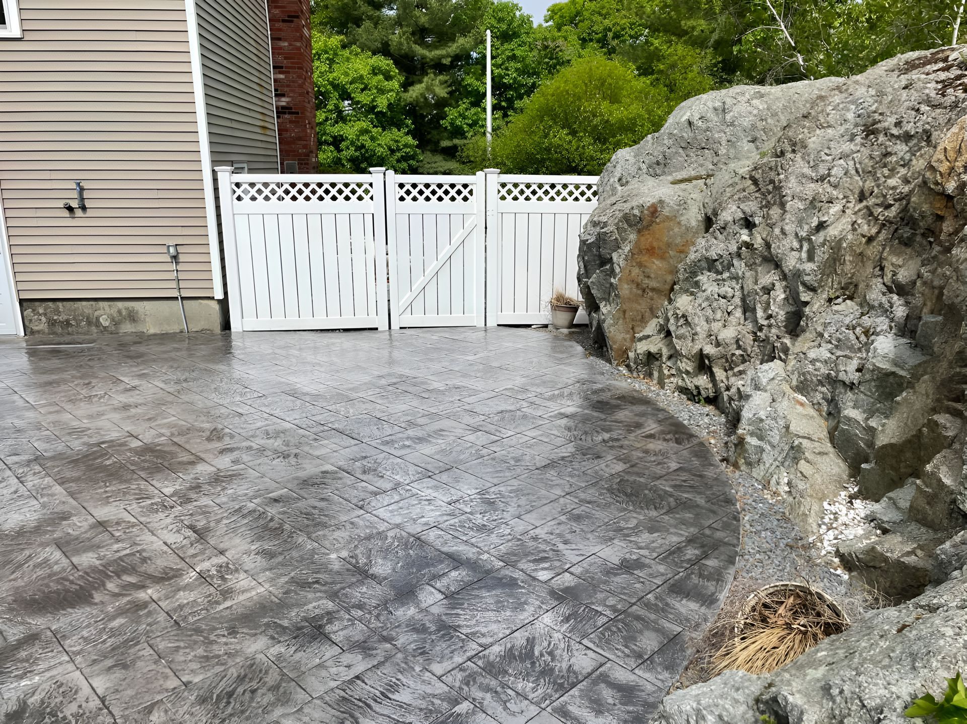 A concrete patio with a white fence and a large rock in the background.