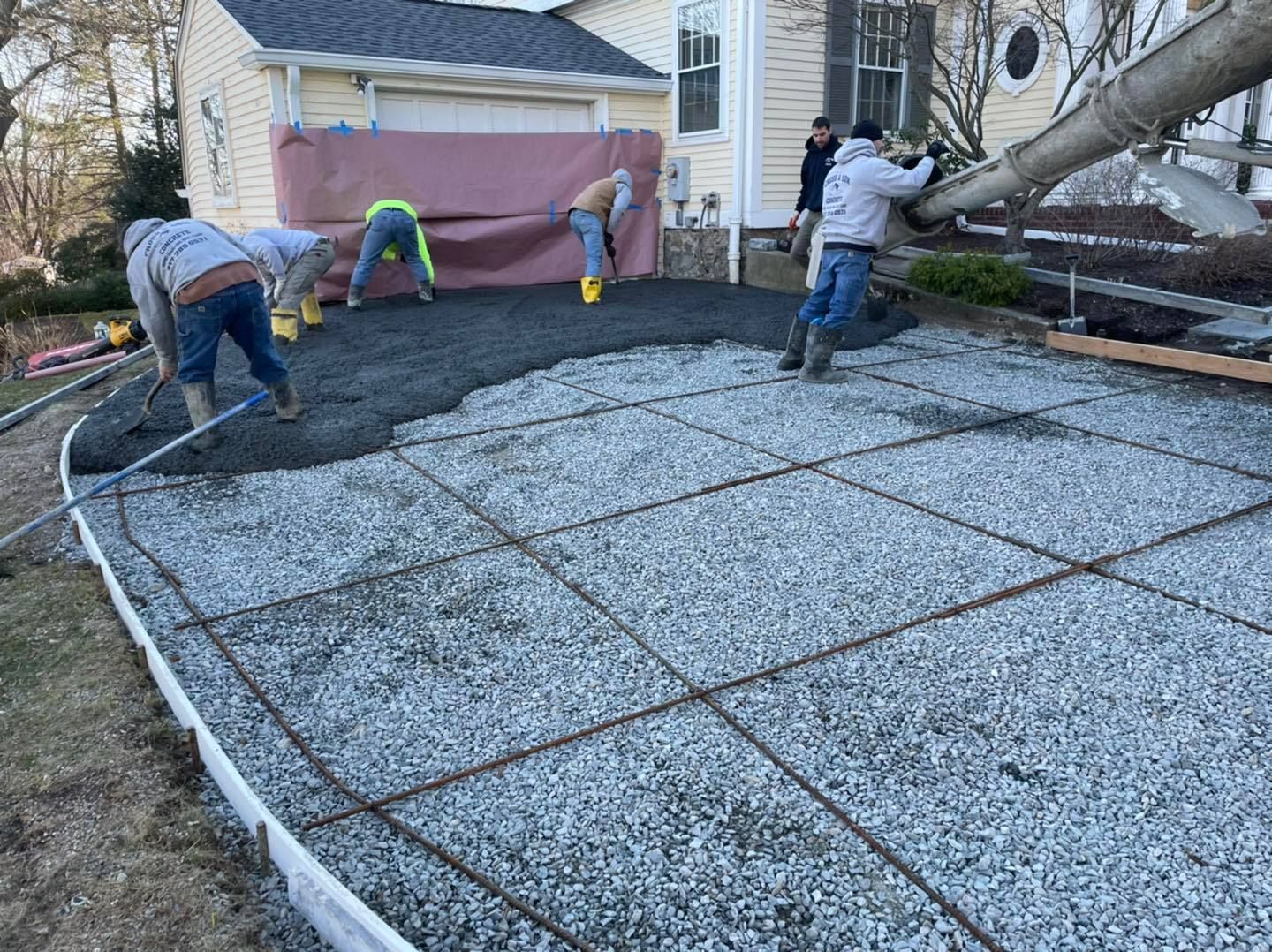 A group of men are working on a concrete driveway in front of a house.
