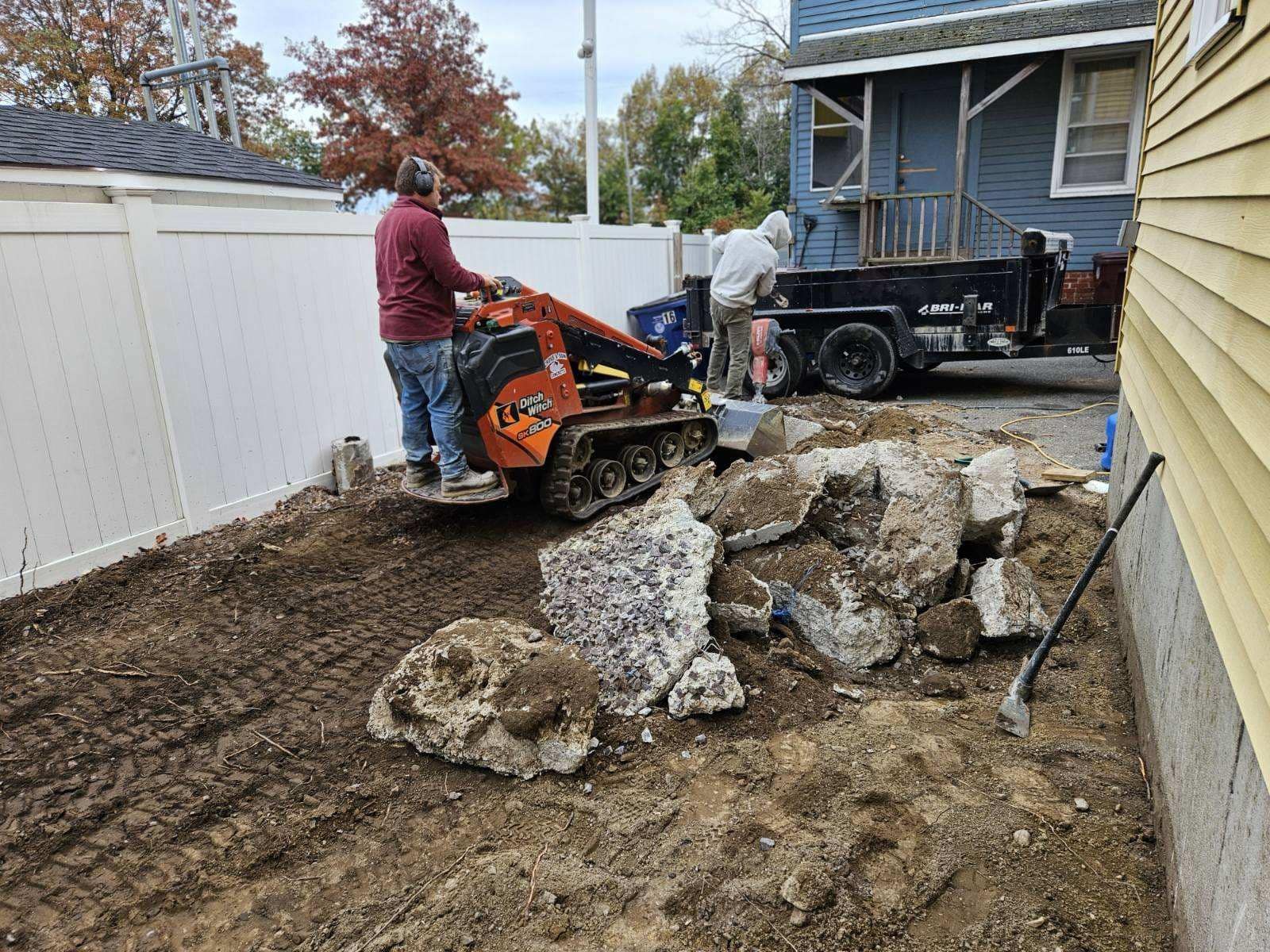 A man is using a tractor to dig a hole in the ground in front of a house.