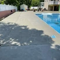 A concrete patio next to a swimming pool with a house in the background.