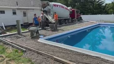 A concrete truck is pouring concrete into a swimming pool.