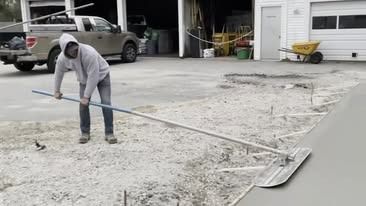 A man is raking concrete in a driveway with a rake.