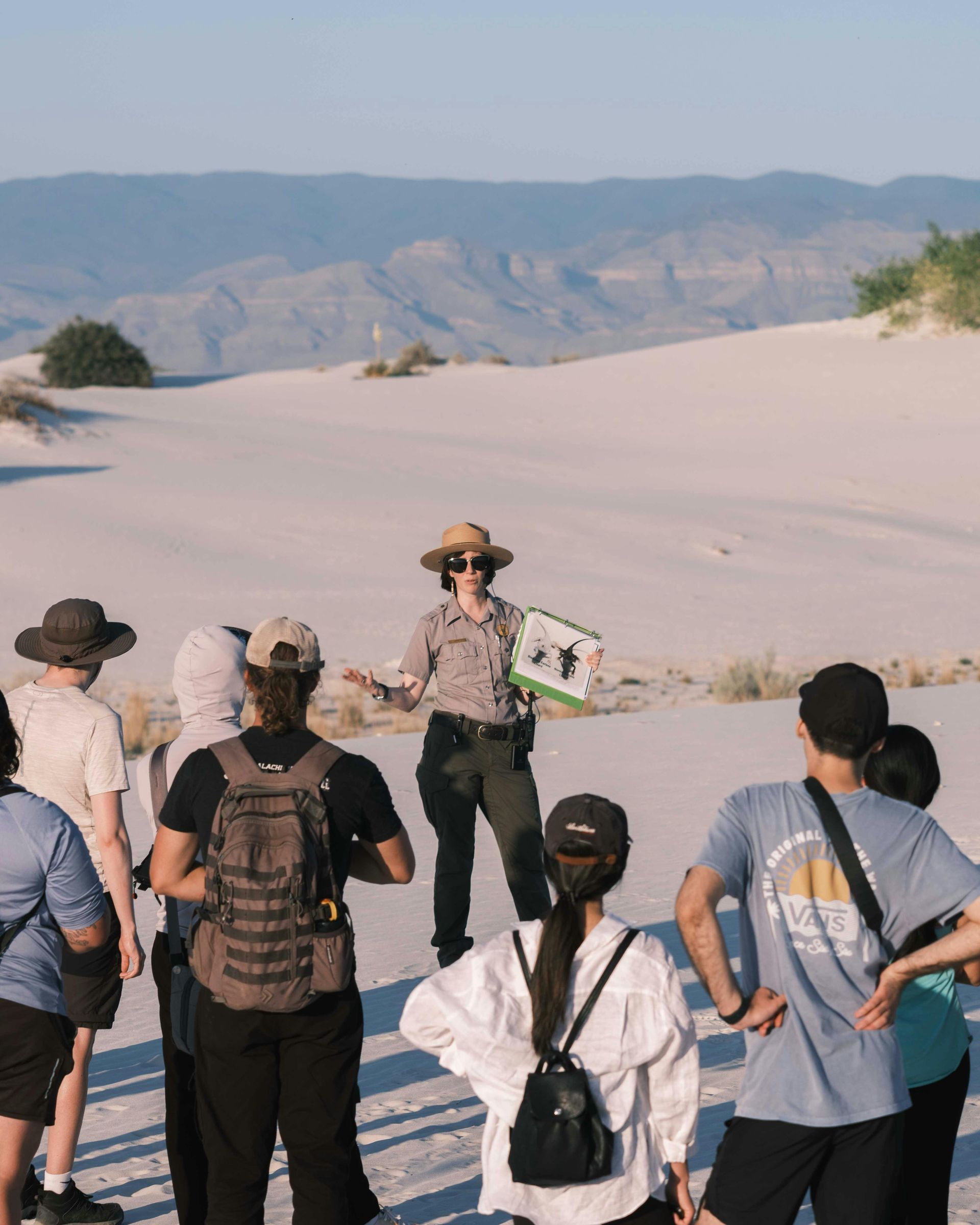 A group of people are standing in front of a sand dune.
