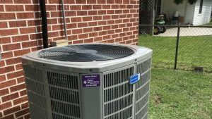 A large air conditioner is sitting on the side of a brick building.
