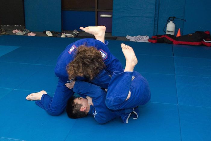 Two people in blue gis practicing jiu-jitsu on a blue mat.