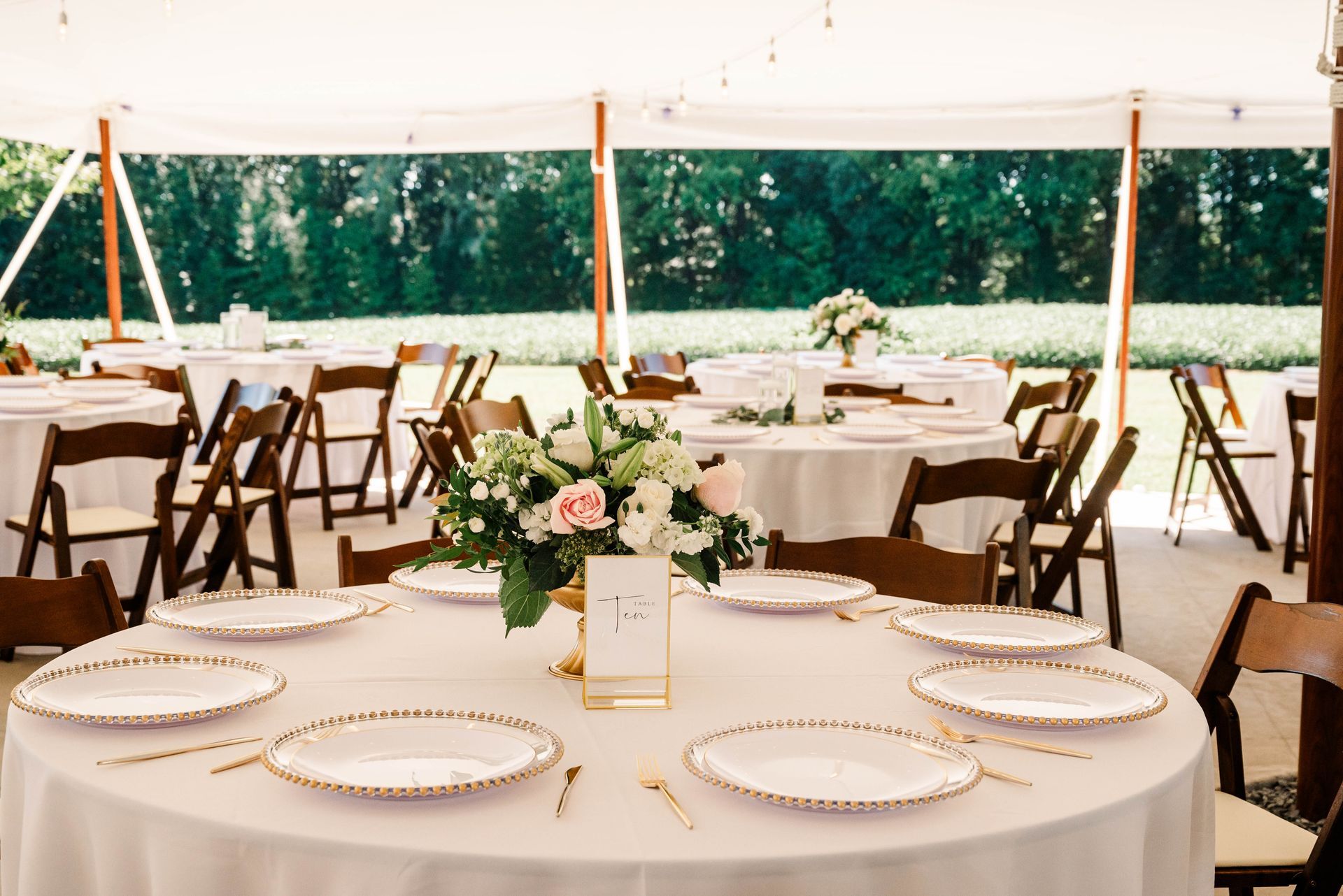 A table set for a wedding reception under a tent with plates and chairs.