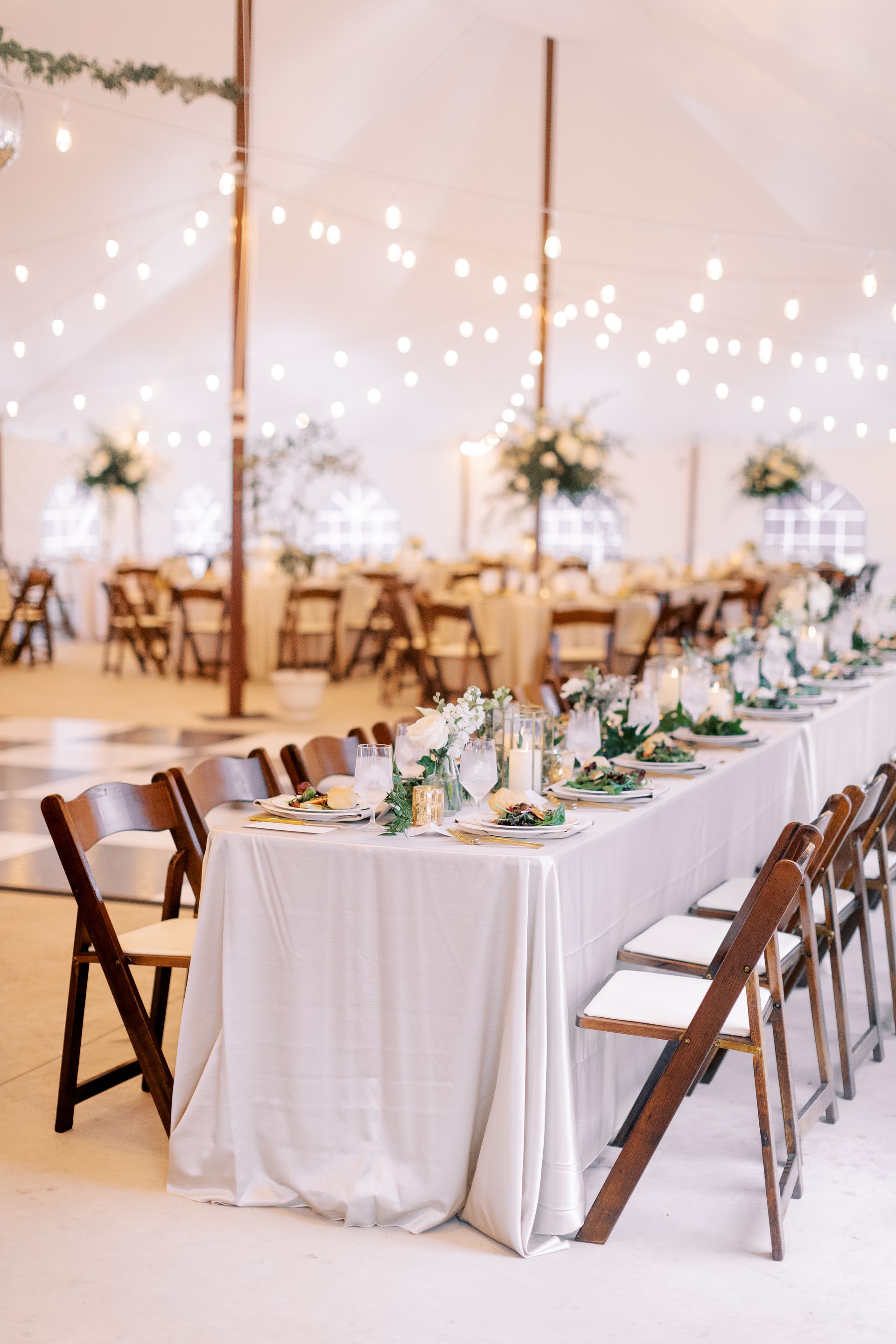 A long table with a white tablecloth and wooden chairs under a tent.