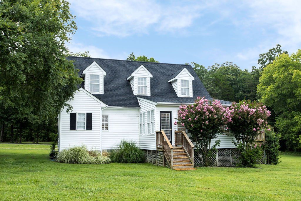 A white house with a black roof is sitting on top of a lush green field.