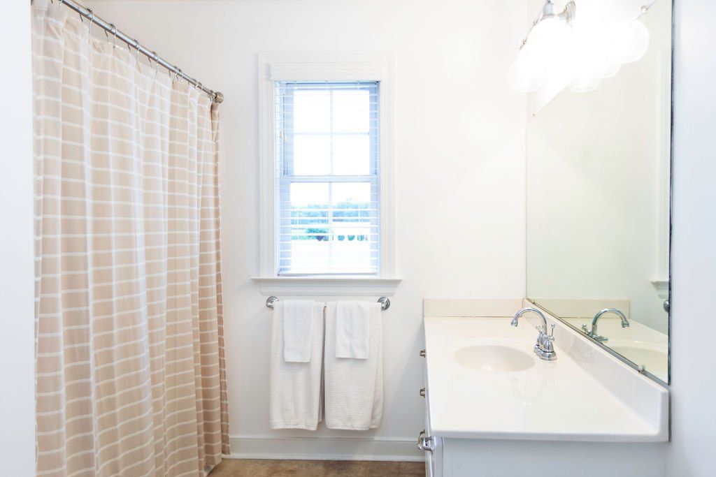 A bathroom with a sink , shower curtain , mirror and window.