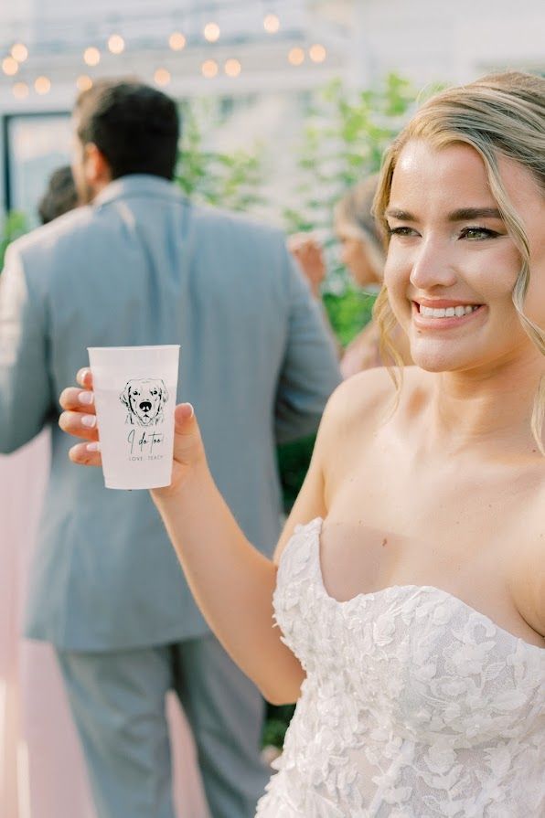 A bride in a wedding dress is holding a cup with a dog on it.