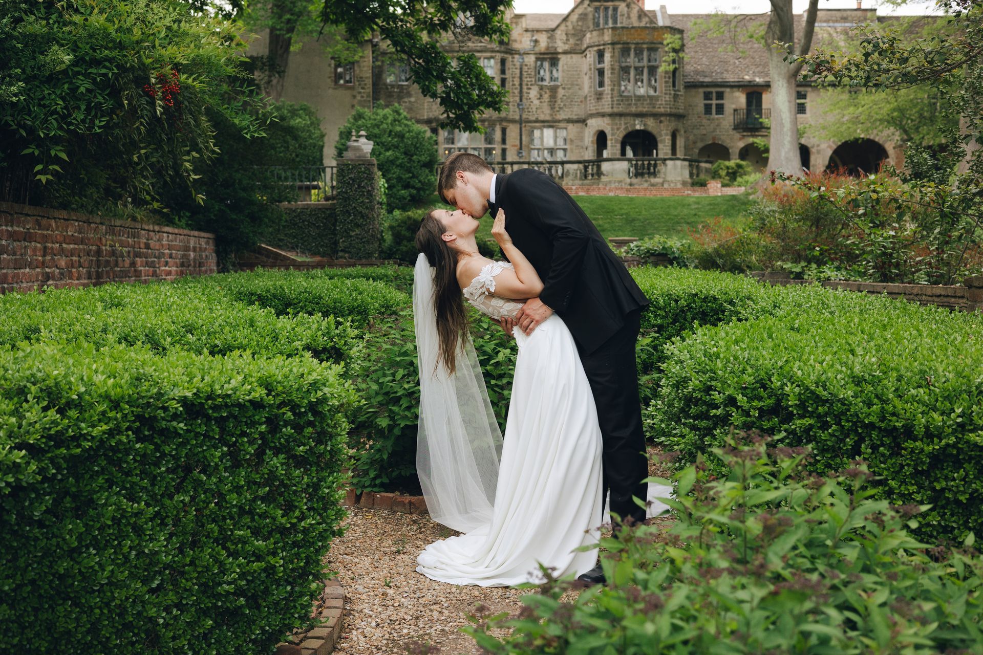 A bride and groom are kissing in a garden in front of a large building.