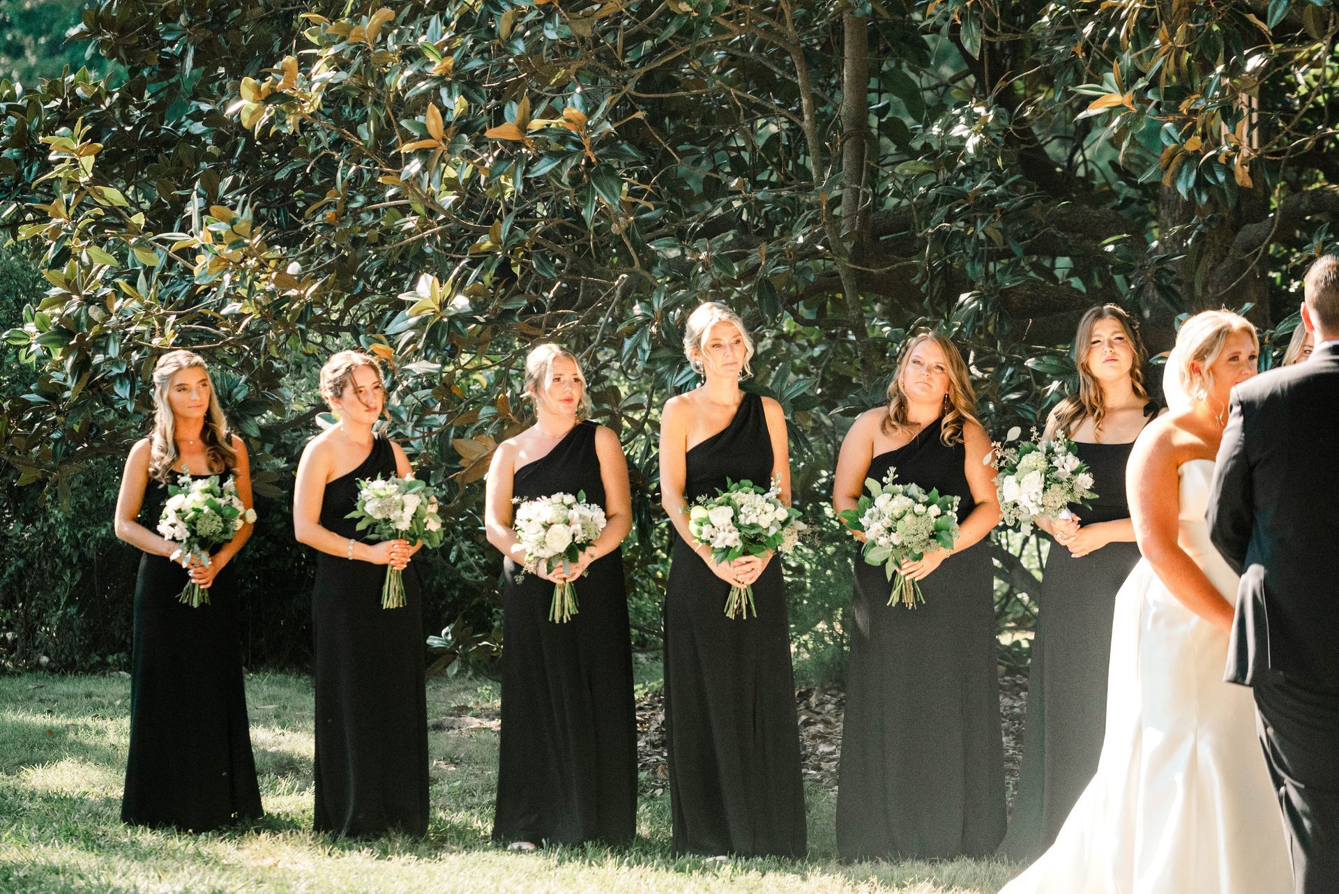 A bride and groom are standing in front of their bridesmaids in black dresses.