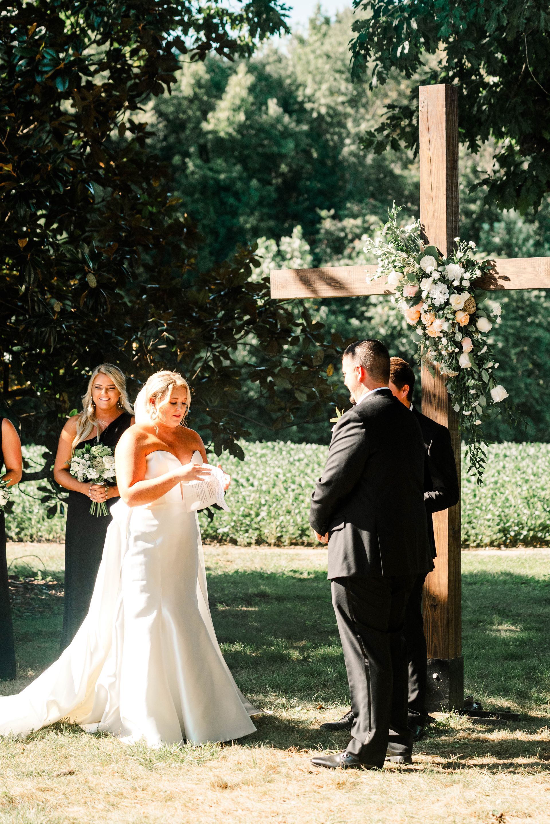 A bride and groom are standing under a wooden cross at their wedding ceremony.