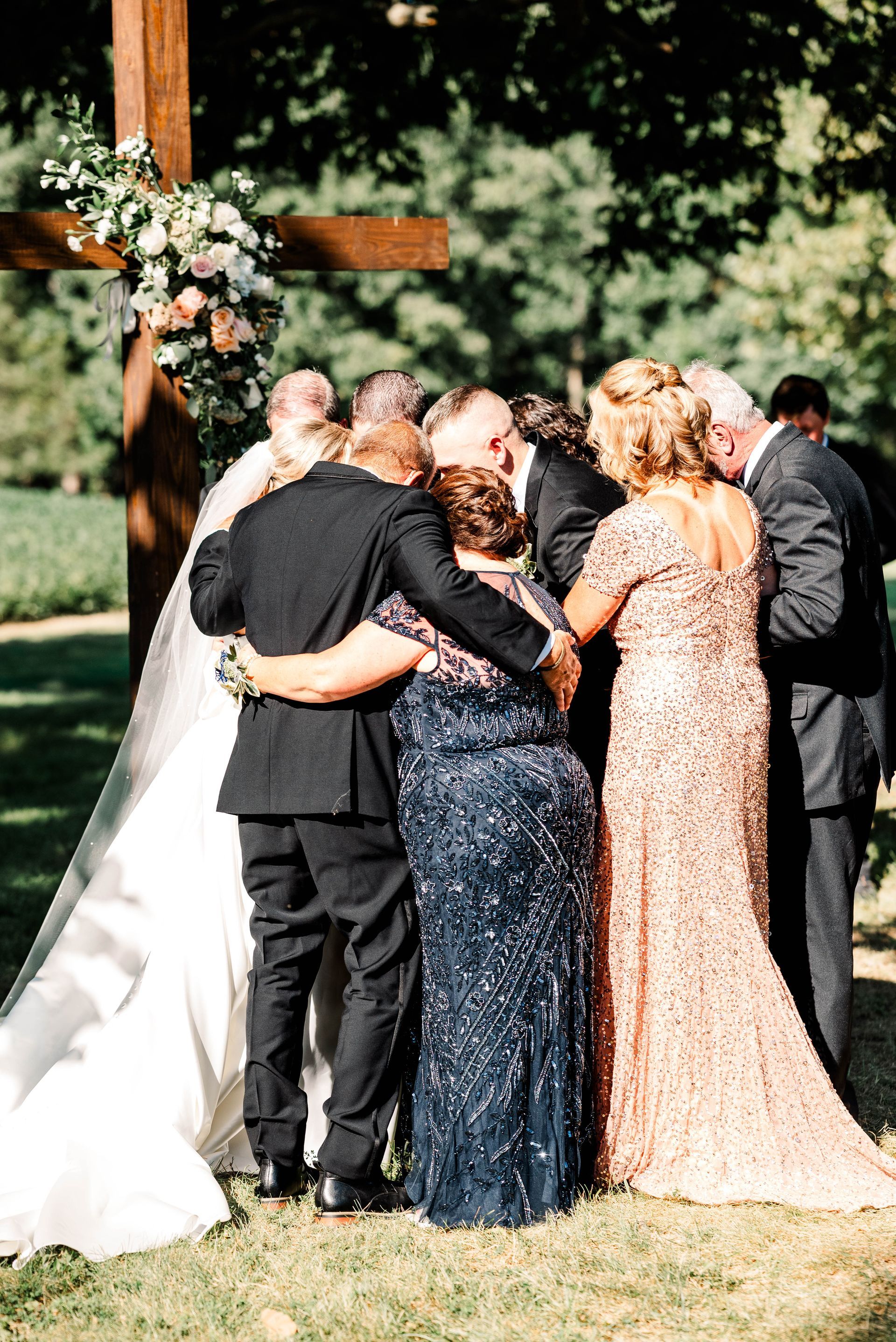 A bride and groom are hugging their parents at their wedding ceremony.