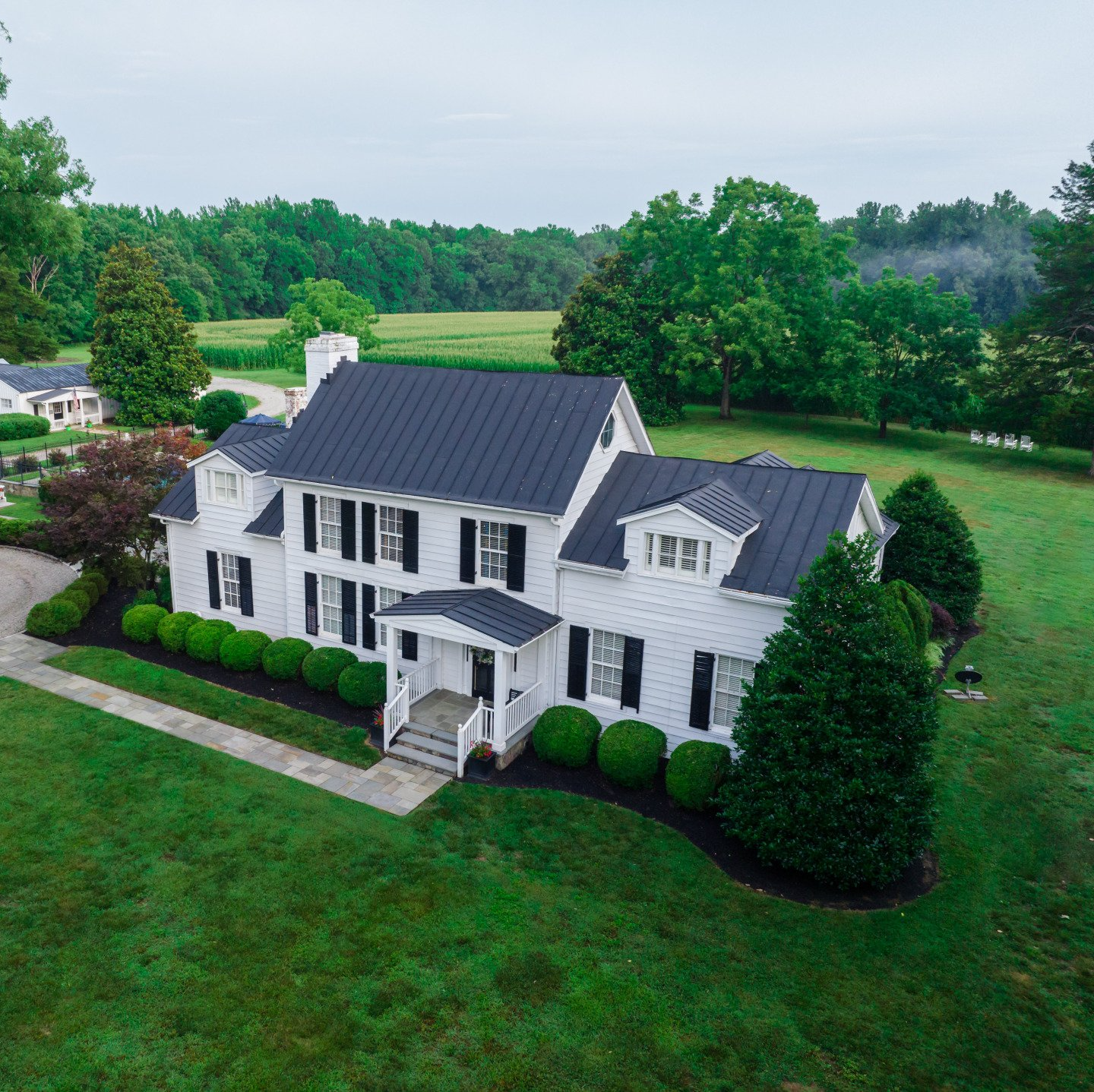 An aerial view of a large white house with a black roof surrounded by trees and grass.