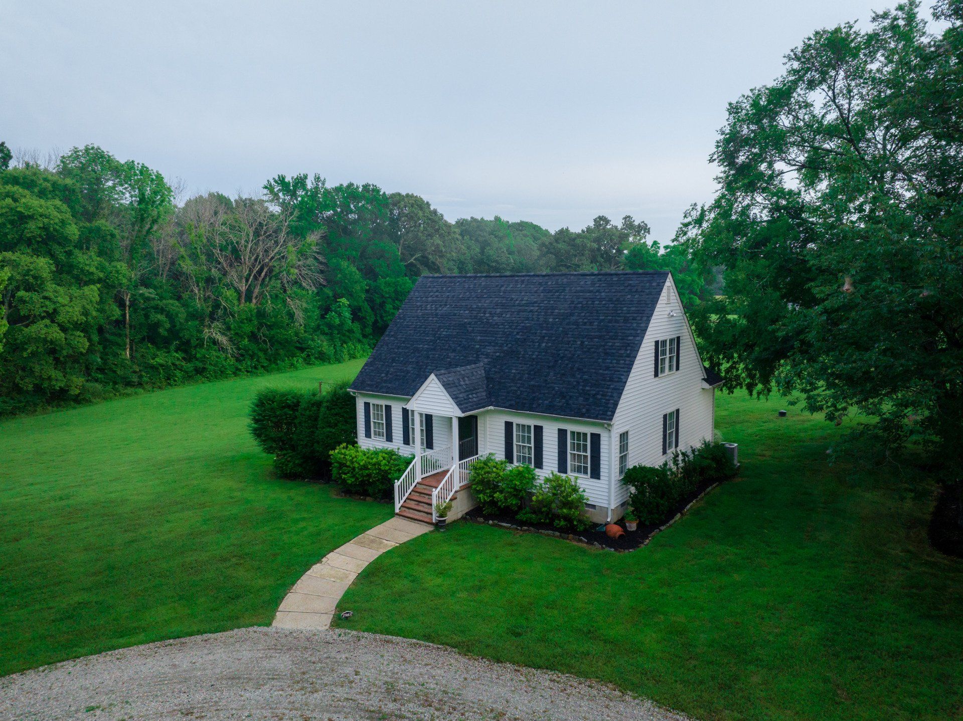 A white house with a blue roof is surrounded by trees and grass.