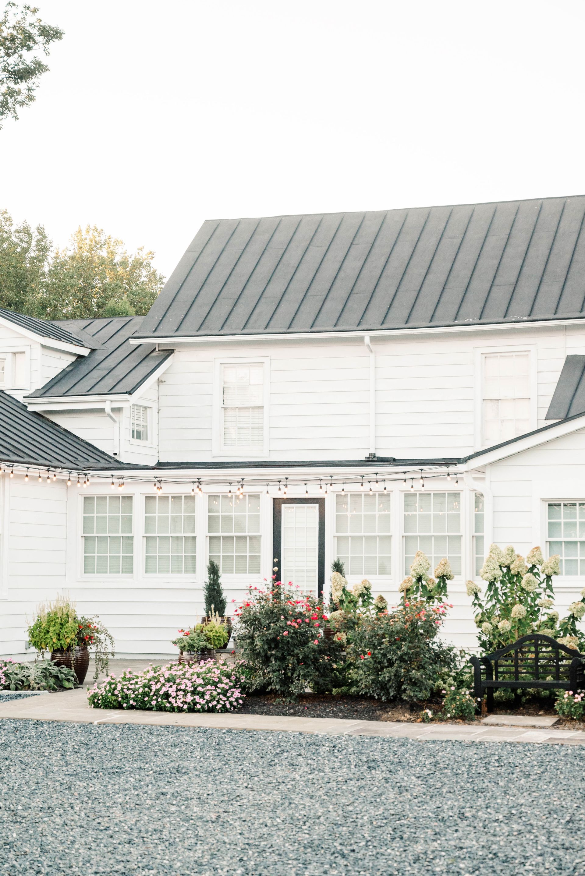 A white house with a black roof and a gravel driveway in front of it.