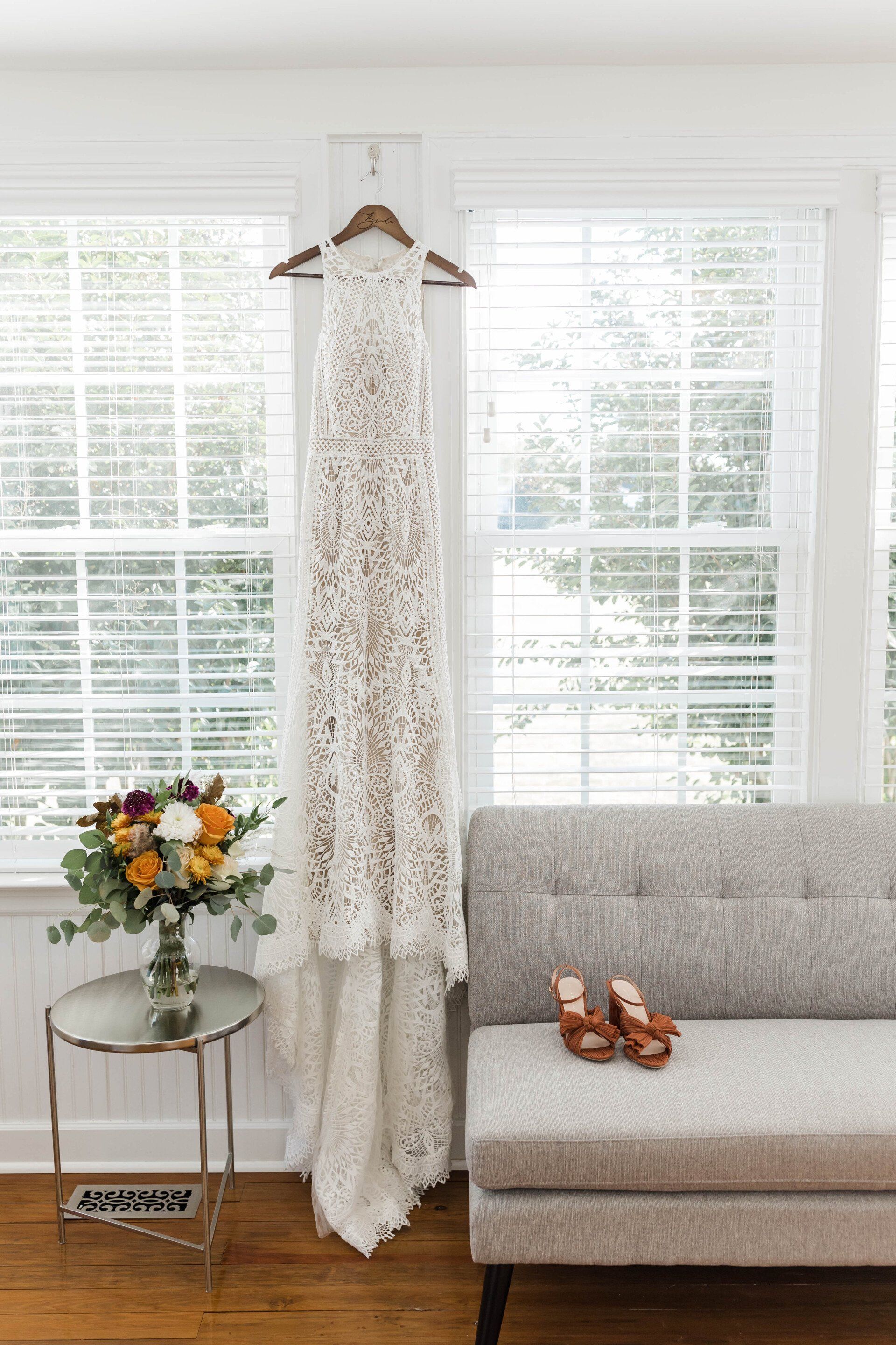 A wedding dress is hanging on a hanger next to a couch.