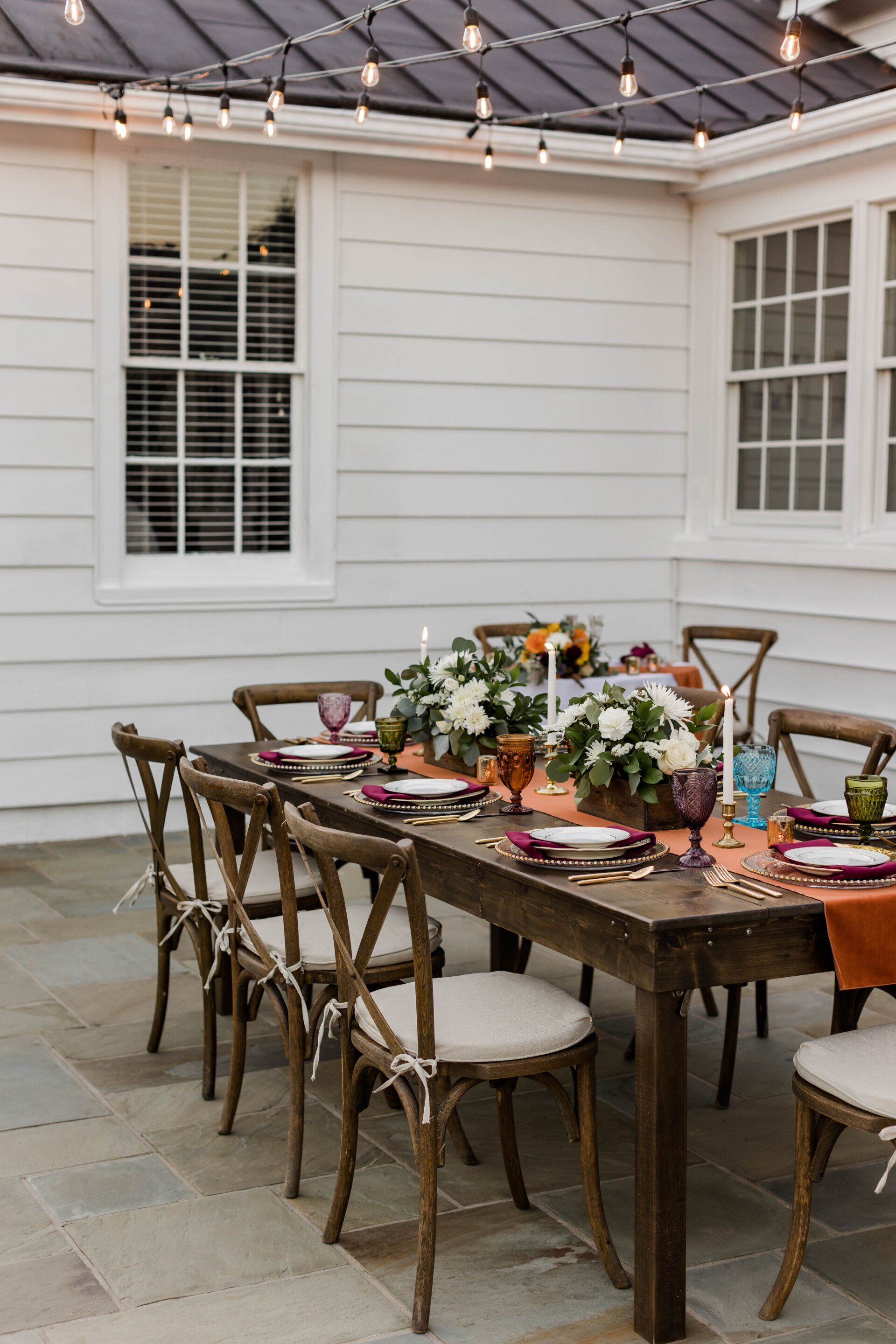 A wooden table and chairs are set for a dinner party on a patio.