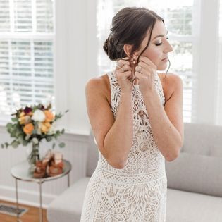 A woman in a white lace dress is putting on her earrings.
