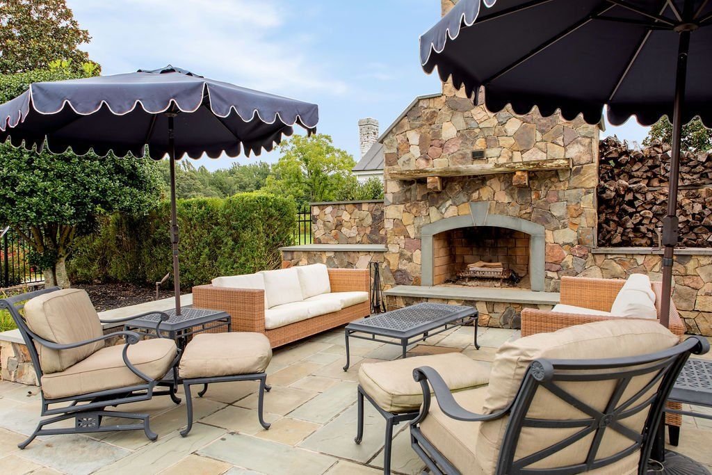 A patio with furniture and umbrellas in front of a fireplace.
