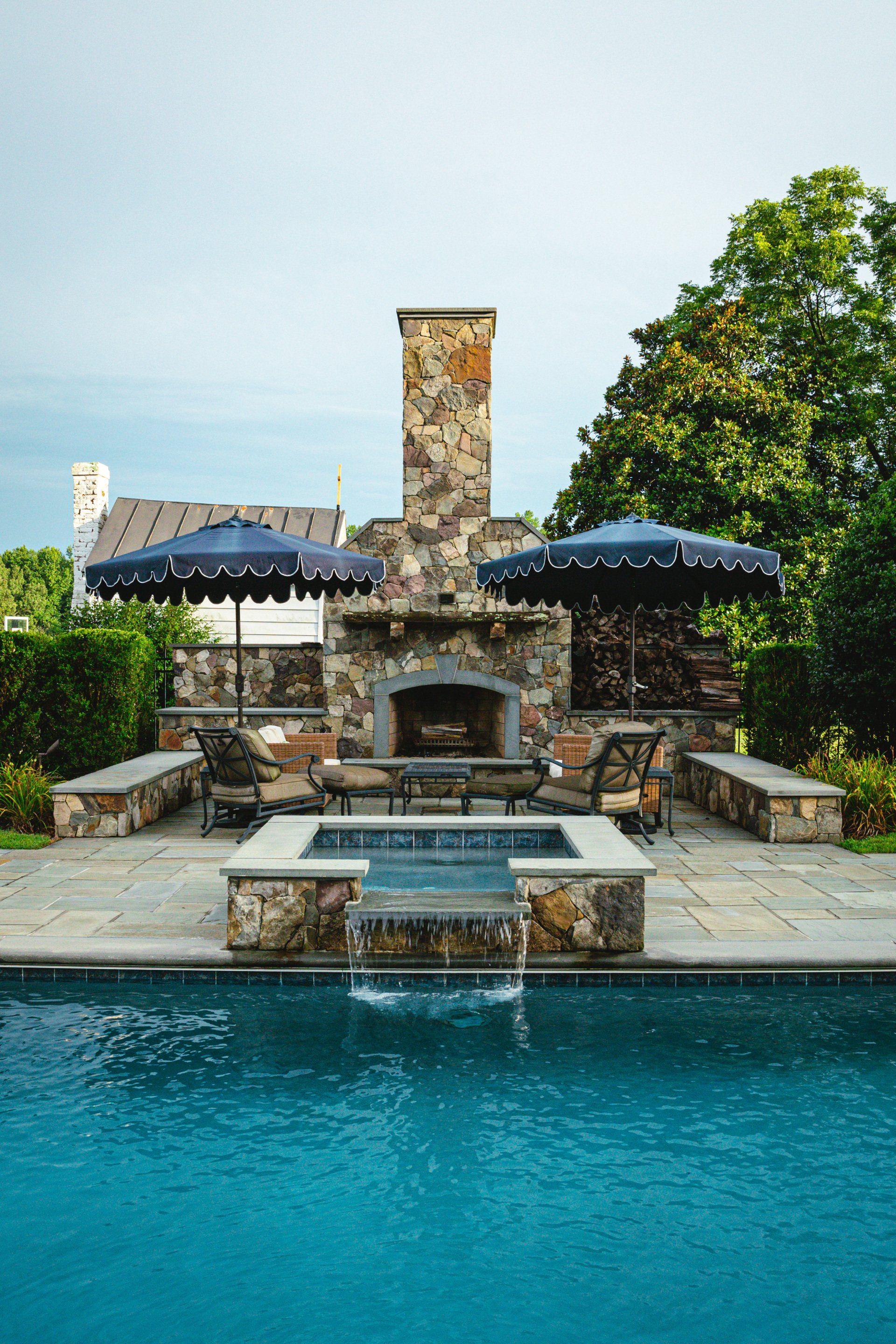 A large swimming pool with a fireplace and umbrellas in the backyard.