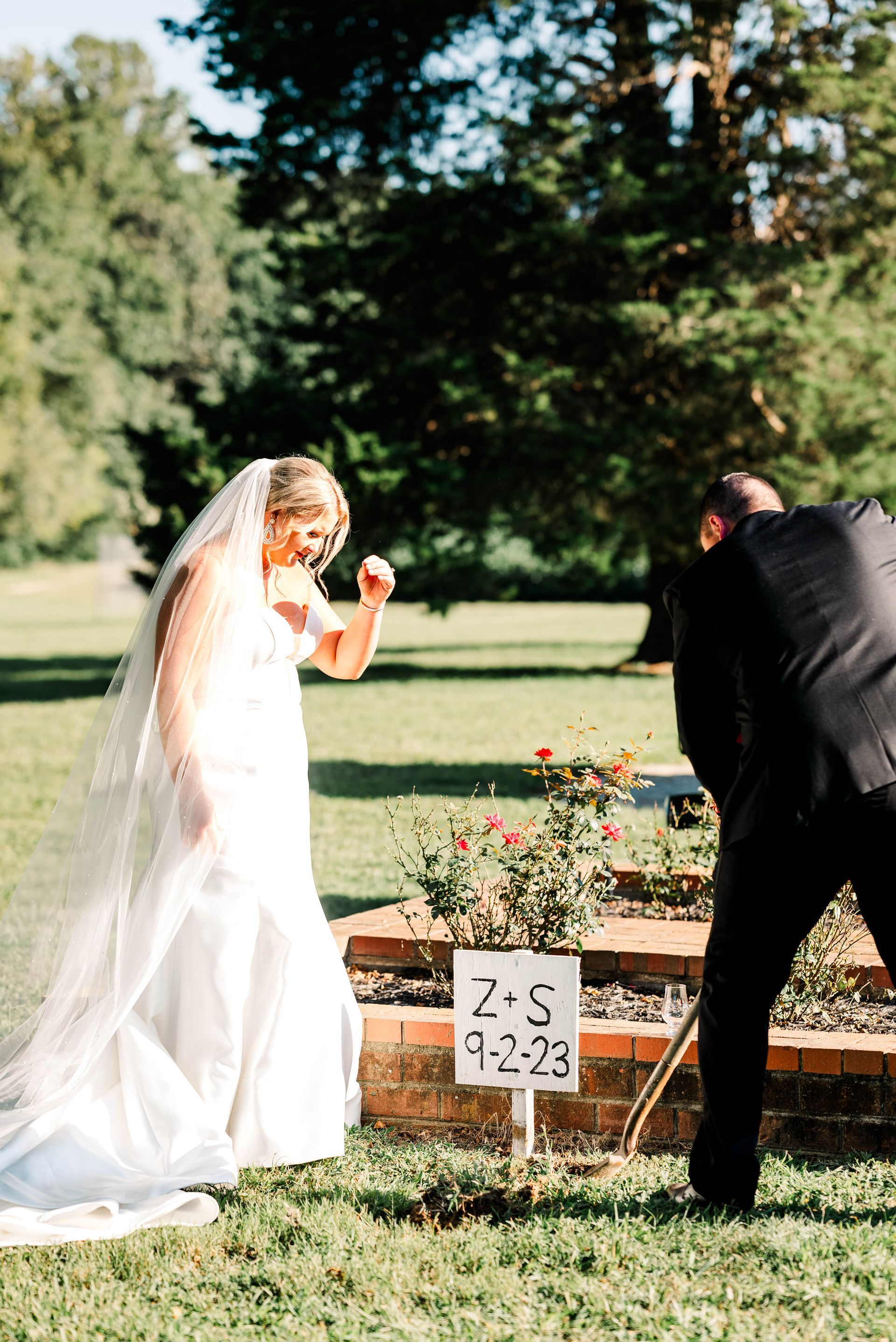 A bride and groom are standing next to a sign in the grass.
