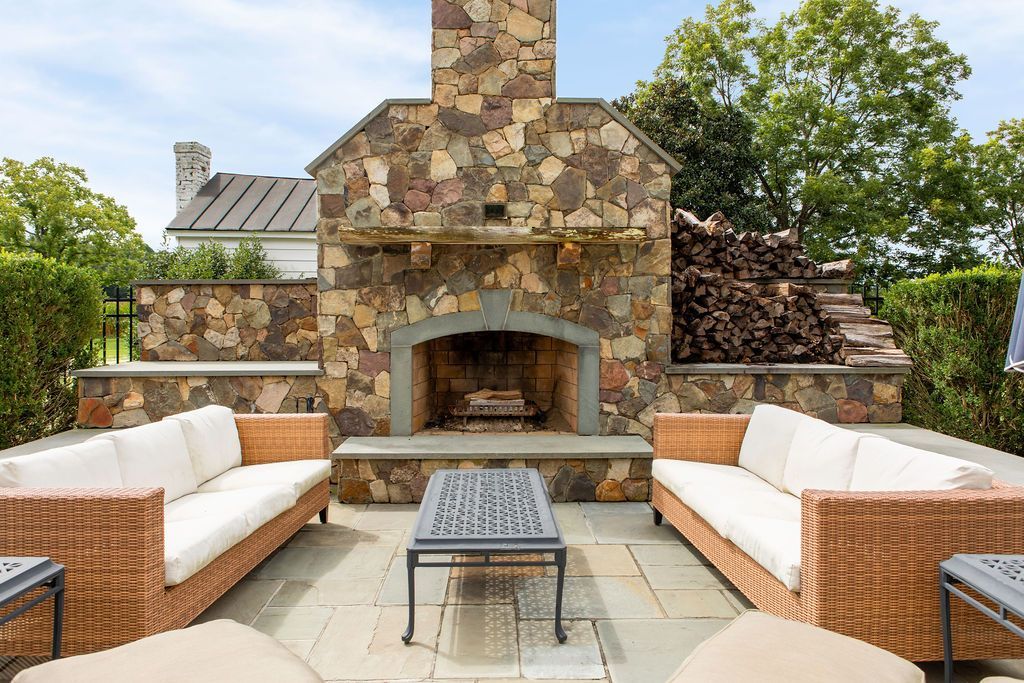 A stone fireplace is surrounded by wicker furniture on a patio.
