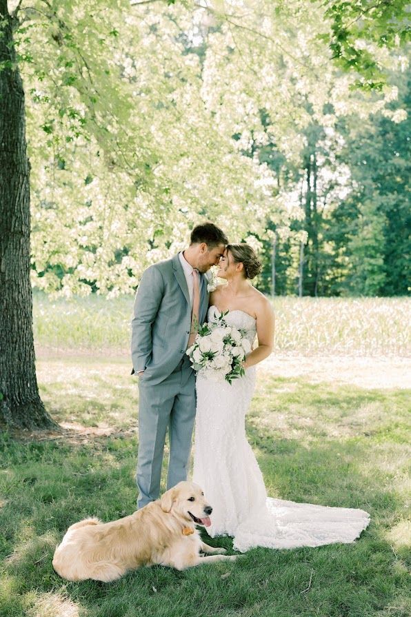 A bride and groom are posing for a picture with their dog.