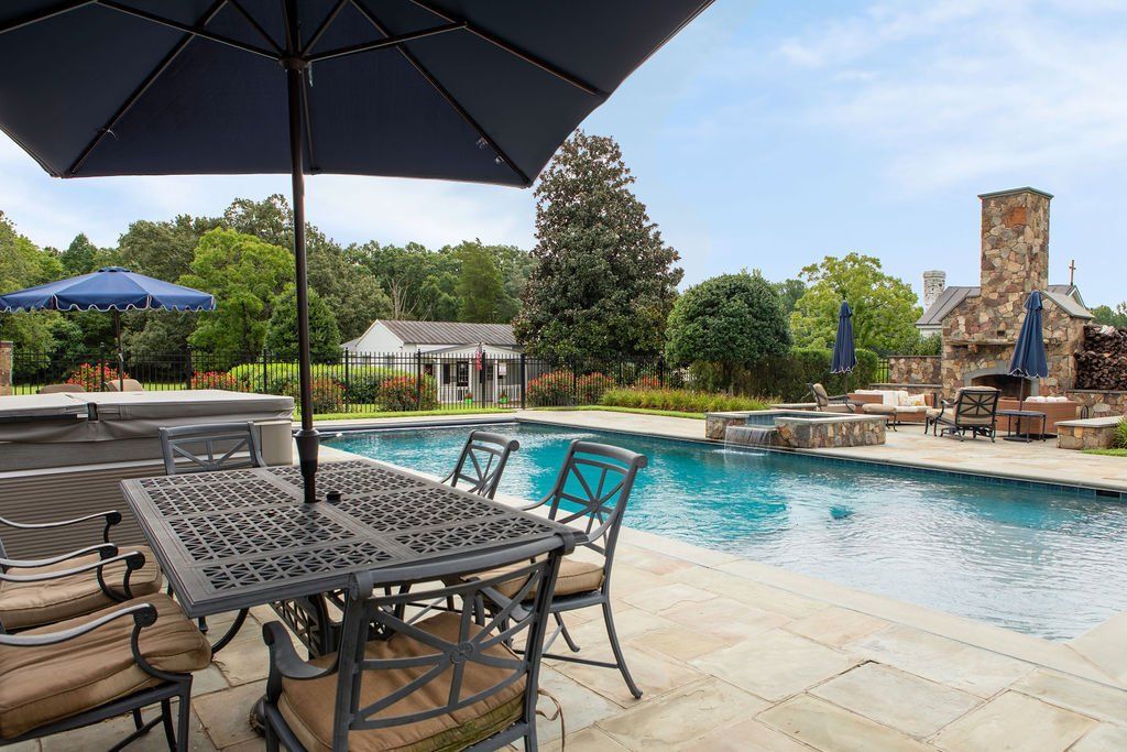 A table and chairs under an umbrella next to a large swimming pool.