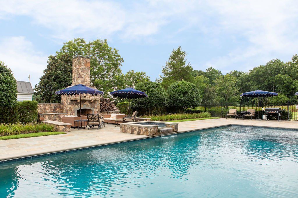 A large swimming pool with a fireplace and umbrellas in the backyard.