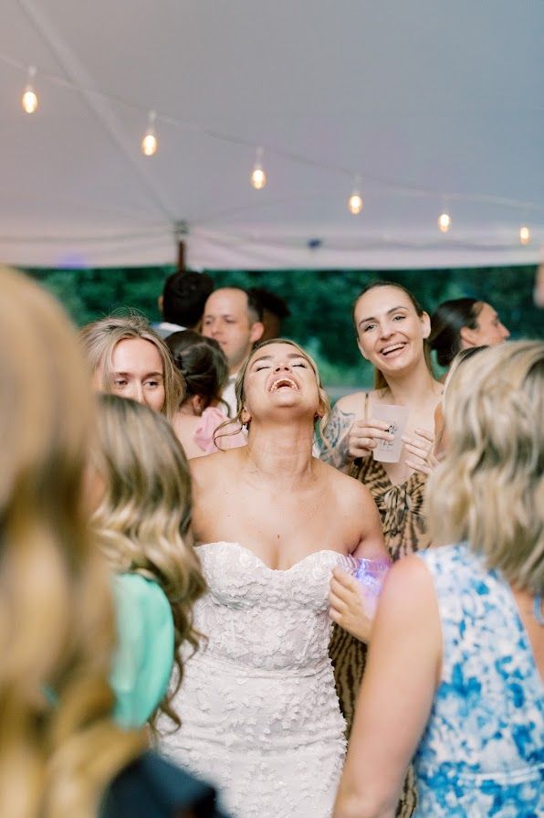 A bride is dancing with her friends at a wedding reception under a tent.