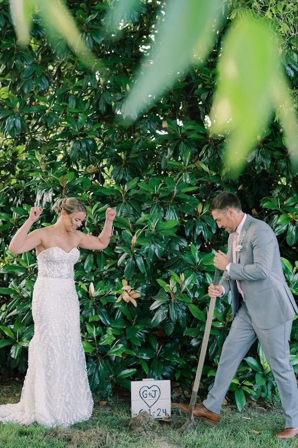 A bride and groom are digging a hole in the ground to plant a tree.
