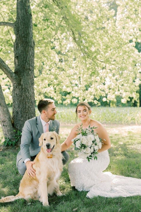 A bride and groom are posing for a picture with their dog.