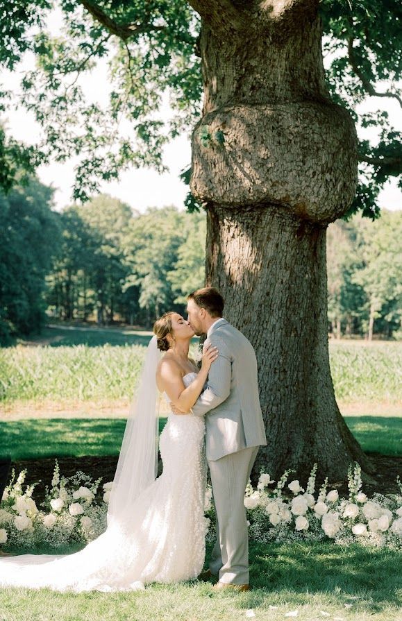A bride and groom are kissing under a tree.