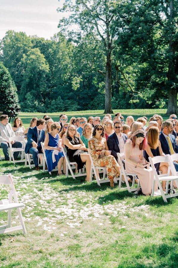 A large group of people are sitting in chairs in the grass at a wedding ceremony.