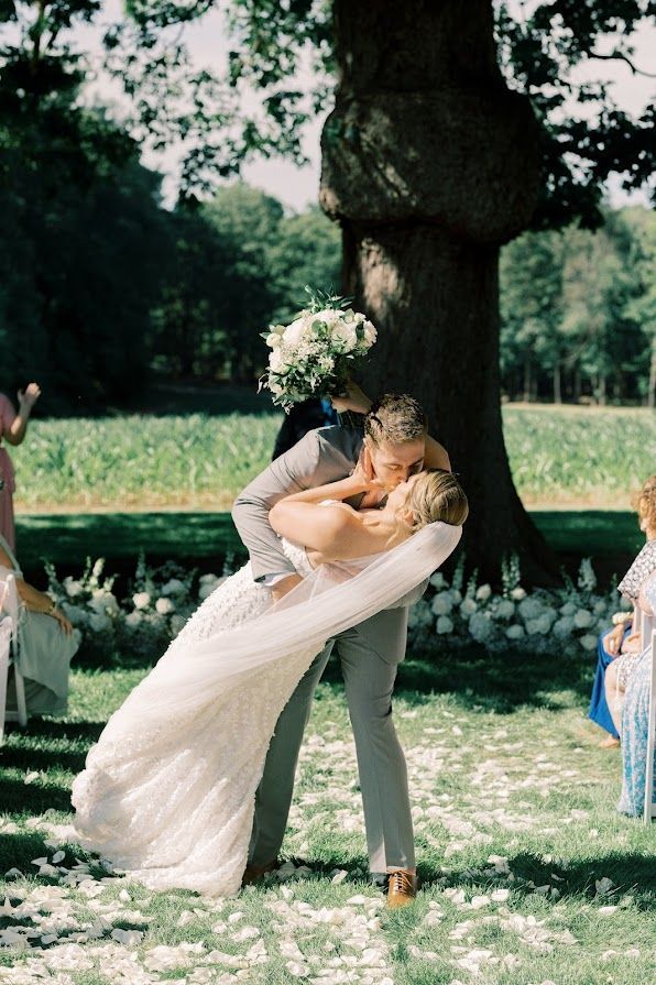 A bride and groom are kissing in front of a tree.