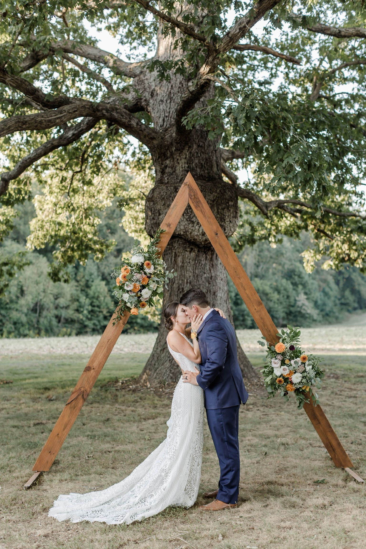 A bride and groom are kissing under a wooden arch.
