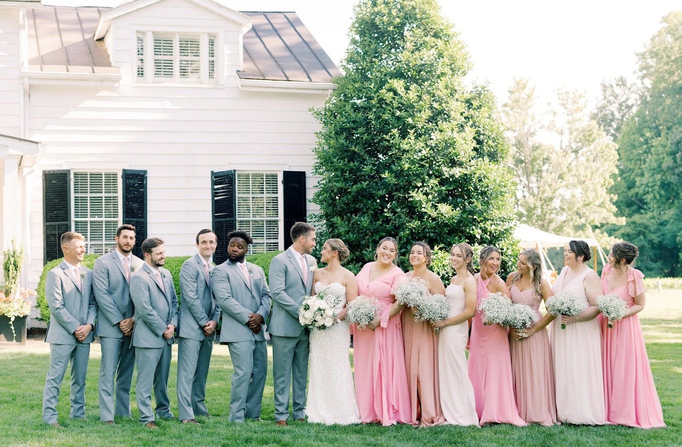 A bride and groom and their wedding party are posing for a picture in front of a white house.