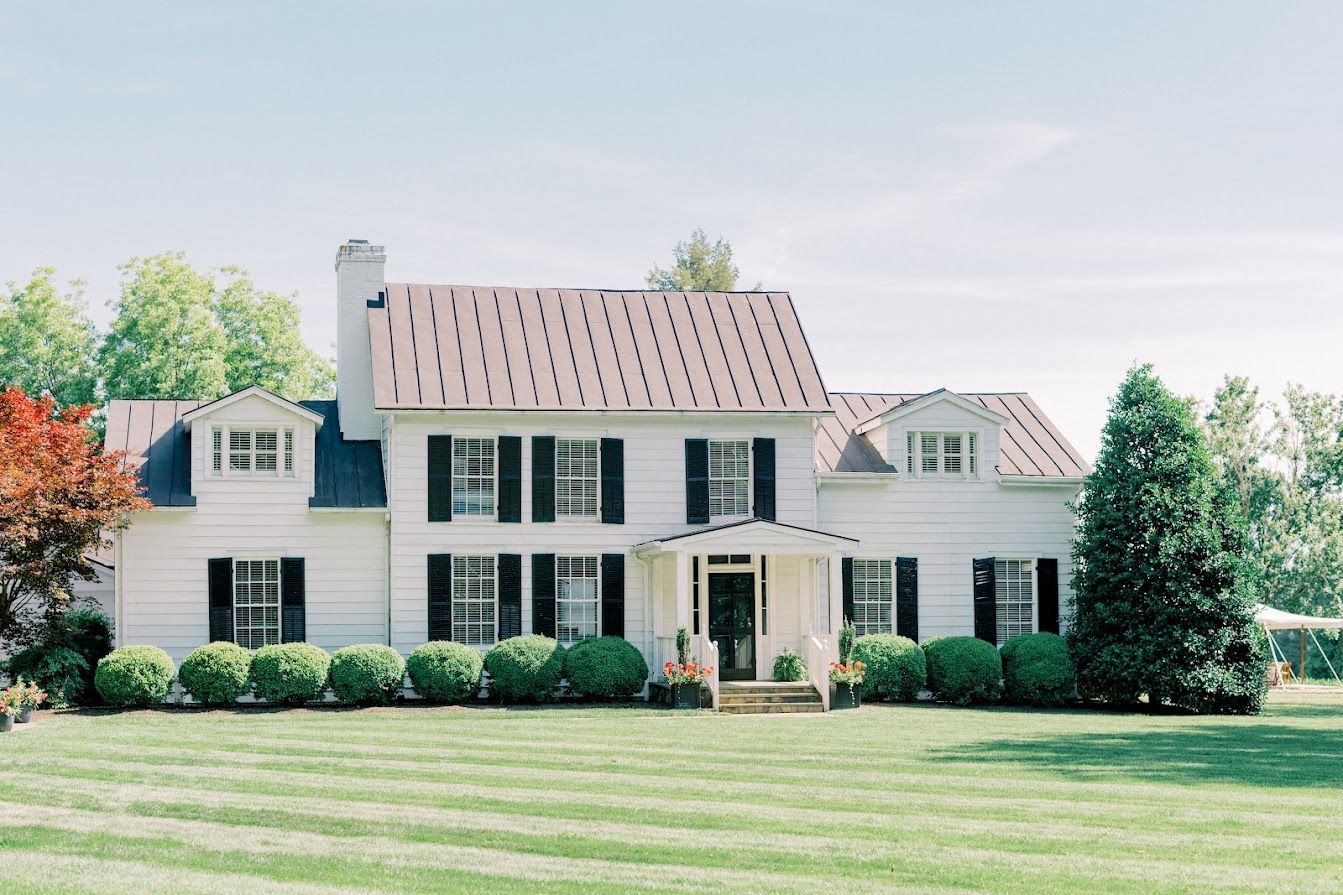 A large white house with black shutters is sitting on top of a lush green lawn.