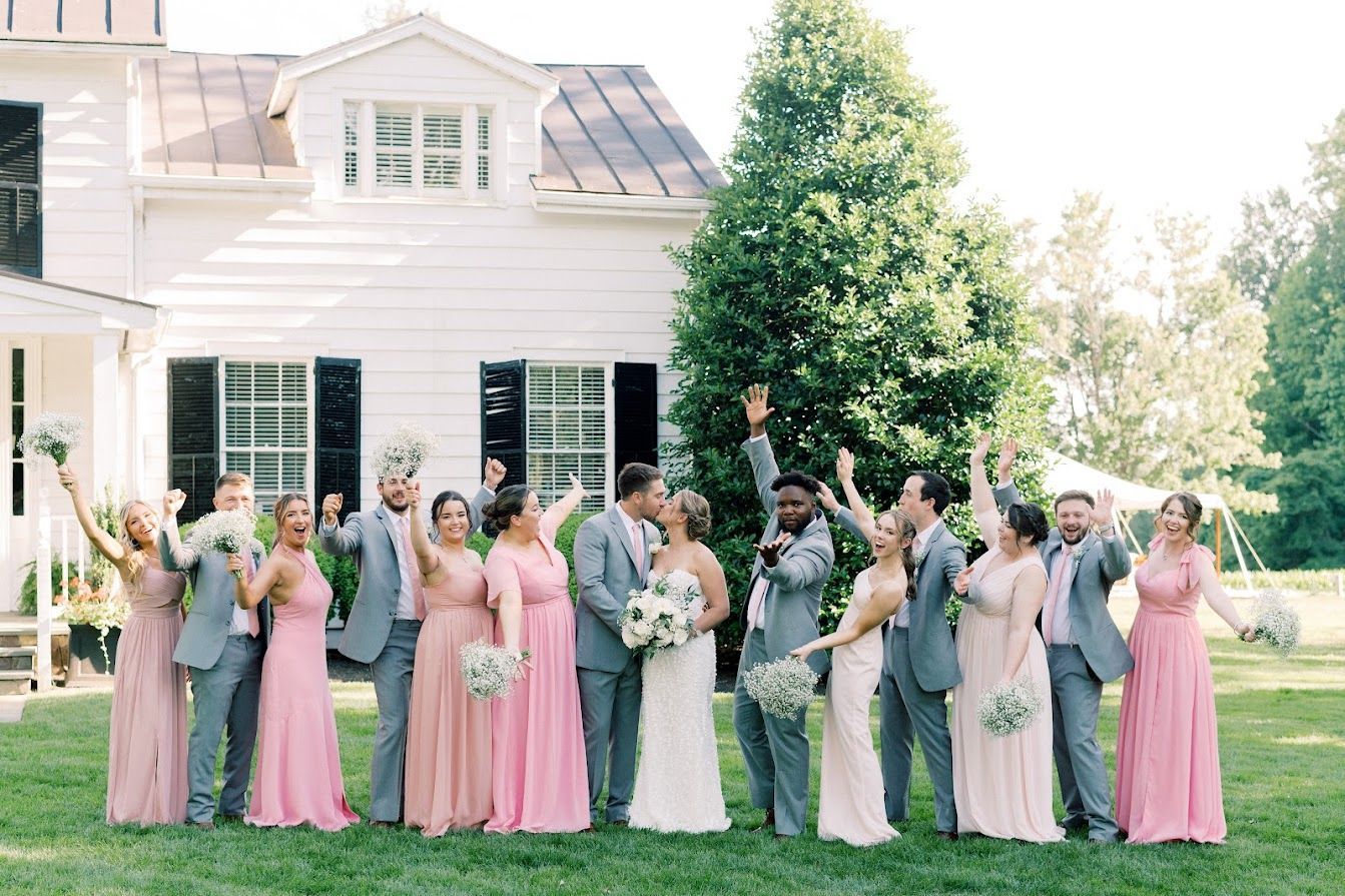 A wedding party is posing for a picture in front of a white house.