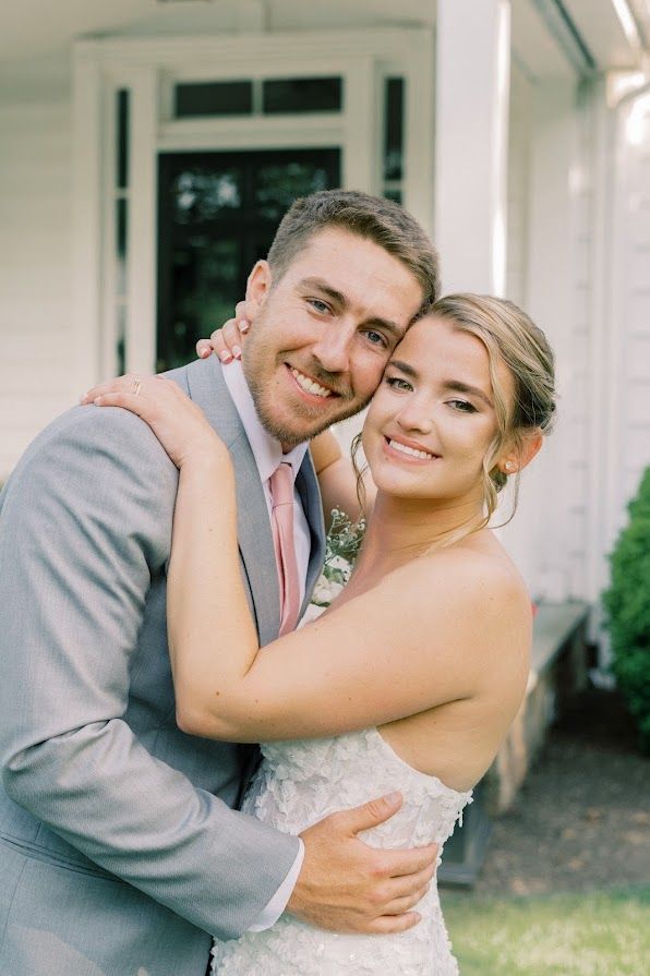 A bride and groom are posing for a picture in front of a white house.