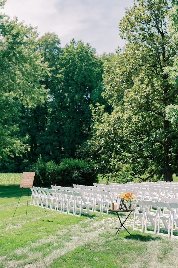 A row of white chairs are lined up in a grassy field.
