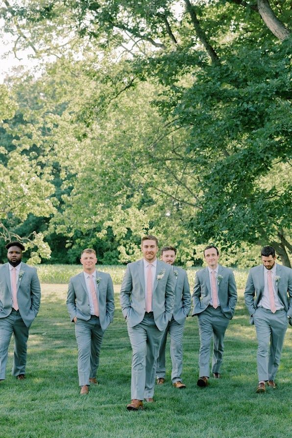 A group of men in suits and pink ties are standing in a field.